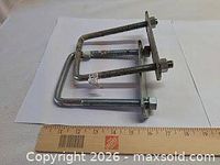 Two galvanized U-bolts with plates beside ruler showing 6-inch length