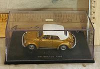 Front left view of gold VW Beetle 1303 model in case, showing label and scale with ruler