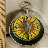 Front of pocket compass beside ruler, showing dial detail and size