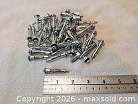 Pile of metal hollow wall anchors beside a ruler showing roughly 2-inch length