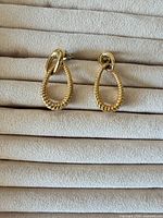 Pair of gold-tone teardrop rope earrings front view on fabric