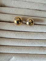 Front view of both gold-tone domed earrings on display pad