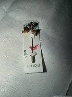 front view of stick pin showing bells and holly on card