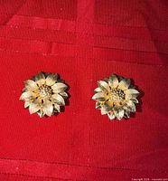 Front view of both gold-tone sunflower clip-on earrings on red fabric