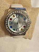 Front view of watch showing dial, rhinestone bezel, coloured crystal markers and white strap