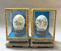 Two signed painted eggs in display cases front view