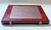 Closed red wood presentation case showing embossed leather insert and brass latches