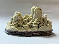 Front view of soapstone mountain village sculpture on wood stand