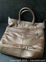 Front view of brown leather weekender bag showing exterior zip pocket and handles