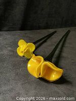 Pair of yellow glass flowers on green stems lying on surface