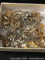 Box filled with mixed gold-tone and silver-tone jewelry pieces, rhinestone accents visible