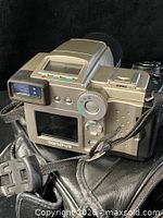 Rear view of Olympus camera showing LCD screen, controls and attached strap on top of carrying case