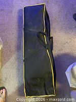 Zippered black carry bag with yellow trim containing tent
