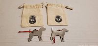 Two pewter dog ornaments laid out with two pouches