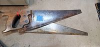 Two overlapping vintage hand saws on floor