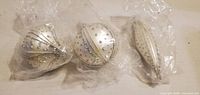 Three white and silver glitter ornaments in plastic wrap