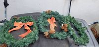 Three green artificial wreaths with pinecones and bows displayed together