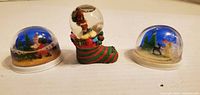 Front view of three snowglobes showing scenes and bases