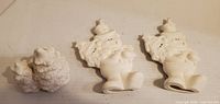 Three unpainted bisque ceramic figures: two Santa Claus, one double tree