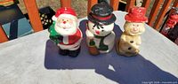 Front view of three wax candles: Santa, snowman with broom, snowman with red hat