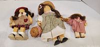 Front view of three wooden dolls with outfits and hats