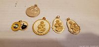 Front view of five gold-tone religious pendants arranged in a row