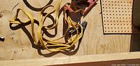 Coiled yellow jumper cable with clamps visible on plywood surface