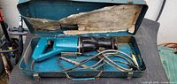 Makita reciprocating saw inside open teal metal case with blades and cord visible