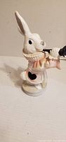 Front view of painted ceramic rabbit figurine holding trumpet and scroll