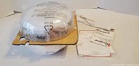 Yogurt maker wrapped in plastic with cardboard spacer beside paperwork