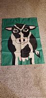 Full view of flag laid flat showing complete cow graphic and green background