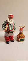 Front view of Santa figurine holding paintbrush beside revolving Santa music box
