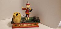 Front view of Trick Dog cast iron mechanical coin bank showing clown, dog, barrel and lettering