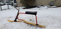 Left side profile of complete snow bike on snow showing frame, skis, handlebar, seat