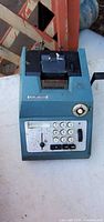 Front view of blue manual printing adding machine showing keypad and paper roll compartment