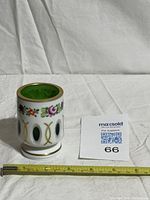 White overlay glass holder with green cut panels, floral and gilt decoration, tape measure for scale