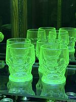 Four tumblers glowing green under UV light, confirming uranium content