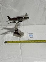 Front angled view of polished aluminum airplane model on stand with measuring tape for scale