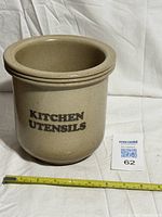 Front view of tan stoneware crock with "Kitchen Utensils" text and measuring tape for scale