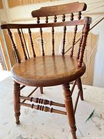 Full view of the wooden captain's chair showing spindle back, turned legs, stretchers, and seat wear
