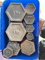 Top view of eight cast iron hexagonal calibration weights showing denominations 1 kg to 100 g and overall condition.