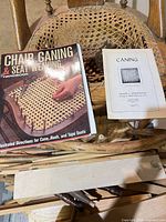 Top view of chair showing broken cane seat, two instruction books, cane reed bundle and wooden tools