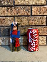 Doll in case beside Coke can for scale