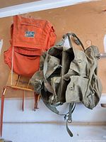 Two external frame backpacks, orange Everest on wooden frame and olive military surplus on metal frame
