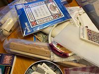 Assortment of needlepoint supplies, kits, tools and magazines spread on table