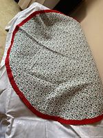 Round holly print tablecloth with red ruffle lying on white cloth