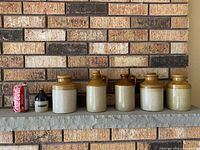 Front view of five stoneware crocks on shelf for size and condition reference