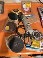 Makita angle grinder with cord and multiple loose sanding discs and packaged accessories in orange tray