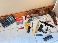 Overview of entire lot on floor: sharpener, revolver, belt/holster, knives, multitools