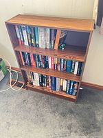 Front view of small brown engineered wood bookcase with three shelves filled with books